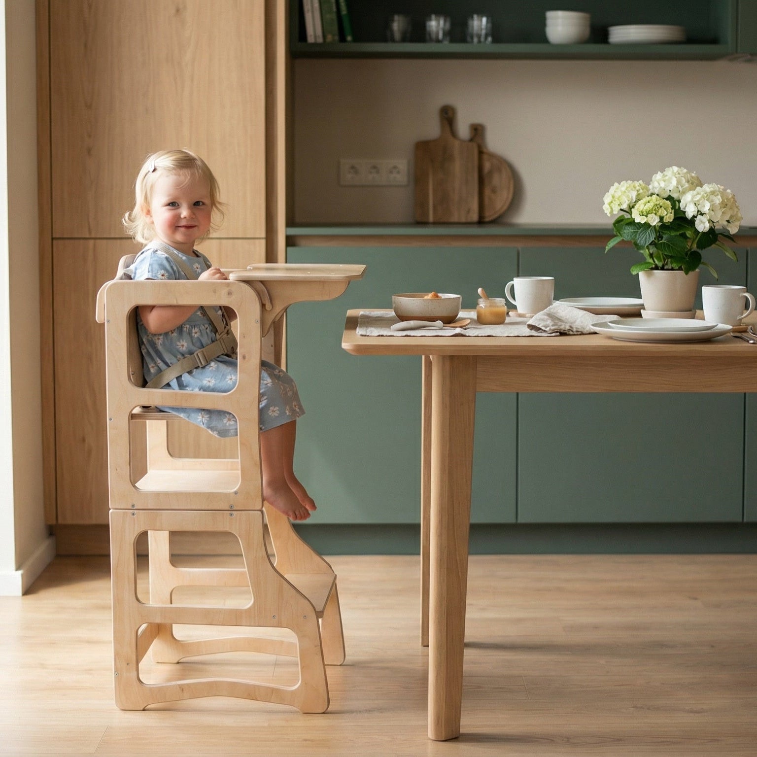 Child in a high chair at a kitchen table with a vase of hydrangea on the table.