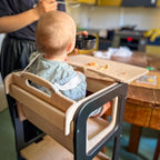Child in a high chair at a kitchen table with a person feeding them.