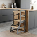Wooden step stool against a kitchen counter with gray cabinets and wooden flooring.